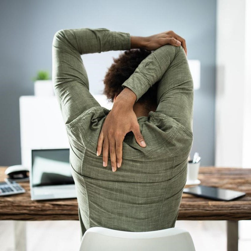 young black woman stretching at her desk, back pain, stretching arm, shoulders, and neck. blog post shows exercises and practices to use to improve your posture and relieve back pain and tension at work, at home, or anywhere